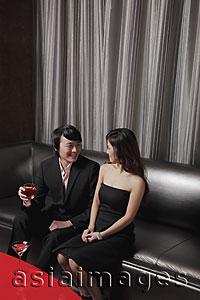 Asia Images Group - Young couple sitting together on sofa smiling at each other