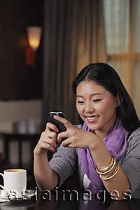 Asia Images Group - Young woman sitting in restaurant holding phone