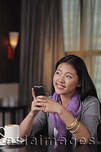 Asia Images Group - Young woman sitting in restaurant holding phone