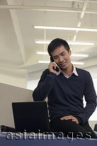 Asia Images Group - Young man talking on phone and working on computer
