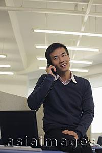 Asia Images Group - Young man sitting on the desk and talking on phone