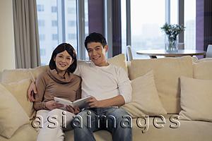 Asia Images Group - Young couple sitting on sofa reading a book