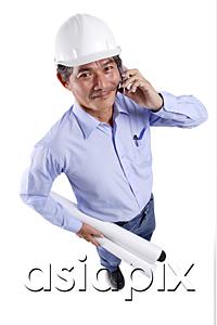 AsiaPix - Mature man wearing construction hat, using mobile phone, carrying blueprints, looking at camera
