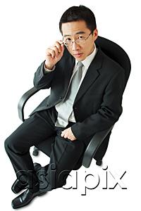 AsiaPix - Businessman sitting on office chair, adjusting glasses
