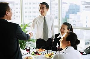 AsiaPix - Businessmen shaking hands over lunch table, businesswomen sitting next to them