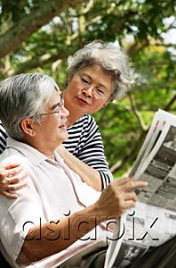 AsiaPix - Senior man reading newspaper, woman behind him