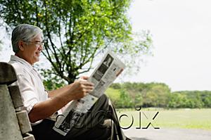 AsiaPix - Senior man sitting on bench in park reading newspaper
