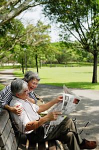 AsiaPix - Couple in park, man reading newspaper, woman standing behind him looking over shoulder
