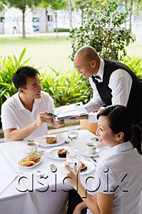 AsiaPix - Couple in restaurant, man handing payment to waiter