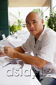 AsiaPix - Man sitting at table, holding cup, looking at camera