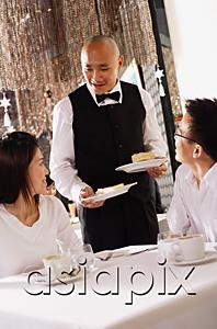 AsiaPix - Couple in restaurant, waiter standing next to their table, holding plates of dessert