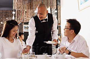 AsiaPix - Couple in restaurant, waiter serving plates of dessert