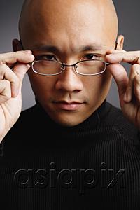 AsiaPix - Man with shaved head, adjusting glasses, looking at camera