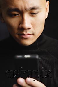 AsiaPix - Man with shaved head, looking at mobile phone, selective focus