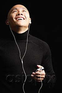 AsiaPix - Man with shaved head, listening to music with earphones, looking up smiling