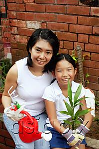 AsiaPix - Mother and daughter, sitting in garden, holding plant and watering can