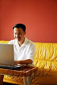 AsiaPix - Man sitting on sofa, using laptop