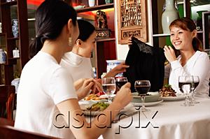 AsiaPix - Three women in restaurant, one woman showing clothing item to the others