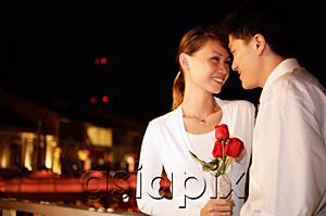 AsiaPix - Couple standing face to face, woman holding single rose stalk, portrait