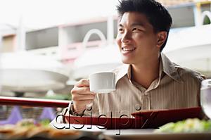 AsiaPix - Man in cafe, menu in front of him, holding cup, looking away