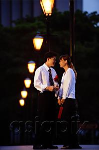 AsiaPix - Couple standing face to face, man holding single rose stalk