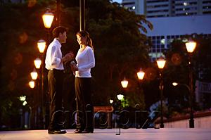 AsiaPix - Couple standing face to face, rows of streetlamps behind them