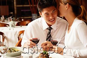 AsiaPix - Couple in restaurant, sitting side by side, woman whispering into man's ear