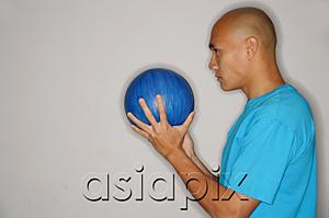 AsiaPix - Man holding bowling ball in front of face, looking away