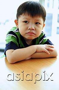 AsiaPix - Young boy looking away, arms crossed, leaning on table