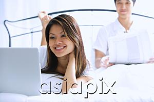 AsiaPix - Couple on bed, woman using laptop, man behind her, reading newspaper