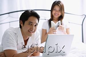 AsiaPix - Couple in bedroom, man using laptop, looking at camera