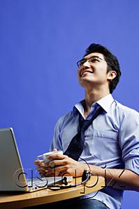 AsiaPix - Man sitting in front of laptop, holding mug, looking up