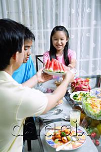 AsiaPix - Father passing food to daughter at dining table