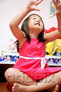 AsiaPix - Young girl sitting cross-legged, looking up, hands raised