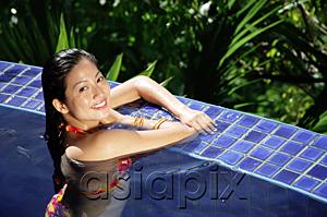 AsiaPix - Woman leaning on edge of swimming pool, smiling at camera