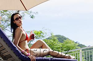 AsiaPix - Young woman in bikini, lying on deck chair, holding drink, turning to look over shoulder