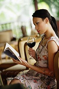 AsiaPix - Woman sitting, holding wine glass, reading a book
