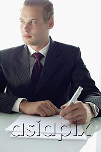 AsiaPix - Businessman sitting at table with pen and paper, looking away