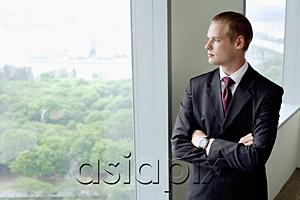 AsiaPix - Businessman standing next to window in conference room, arms crossed