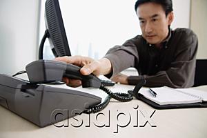 AsiaPix - Male executive sitting at office desk, reaching for telephone