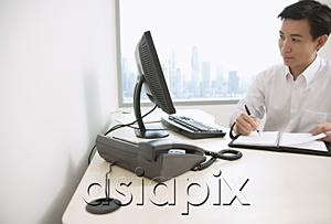 AsiaPix - Male executive sitting at office desk, writing in organizer, looking away