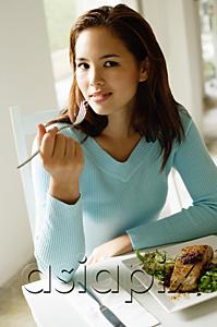 AsiaPix - Young woman sitting at table, food in front of her, looking at camera