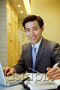 AsiaPix - Businessman with laptop open on table, smiling at camera