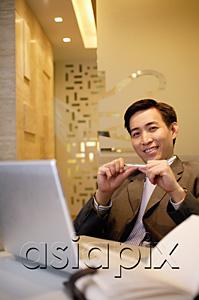 AsiaPix - Businessman sitting, holding pen and smiling at camera
