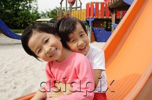 AsiaPix - Two young girls sitting on slide, embracing, smiling at camera