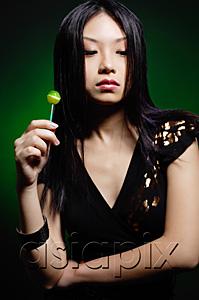 AsiaPix - Young woman in black dress, holding green lollipop, arms crossed
