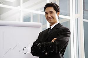 AsiaPix - Businessman standing next to flipchart, smiling, arms crossed