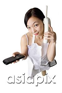 AsiaPix - Woman in apron using cordless phone, holding remote control
