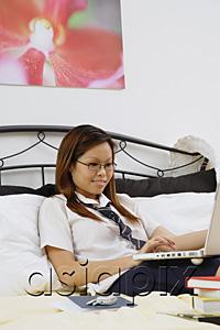 AsiaPix - Girl sitting on bed, using laptop
