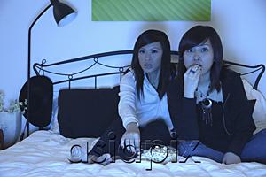 AsiaPix - Two girls in bedroom, watching TV and eating popcorn